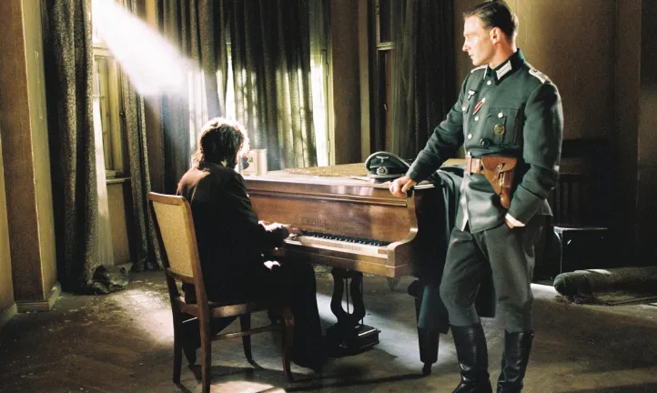 Un homme est assis en face d'un piano, un autre homme debout l'écoute